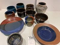View of all twelve pottery items including bowls, plates, and vase arranged on a flat surface.