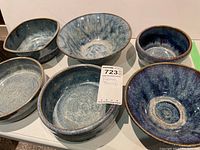 Photo showing six pottery bowls on white surface, varying blue shades and sizes