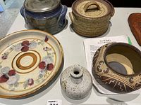 Full view of all five pottery items on table: two bean pots with lids, decorative plate, tall reproduction pot by David Salks, small white vase.