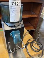 Front view of the Rancilio Rocky coffee grinder showing the clear hopper with coffee beans, grind adjustment dial, and blue metal spout.