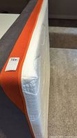Side and top corner view of white quilted memory foam mattress with orange trim and grey underside