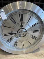 Wall clock showing full face with Roman numerals and brushed metal background, clock hands at 12:45.