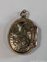 Front view of the oval silver locket pendant showing carved floral and bird design.