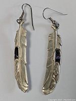 Front view of pair of silver feather-shaped earrings with black inlay and Haida pattern.