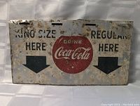 Front view of the 1960s Coca-Cola metal sign displaying wear, rust spots, and fading on the directional text and logo.