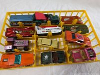 Top-down photo of 12 different die cast cars and trucks in a yellow plastic organizer tray, showcasing various classic toy vehicles.