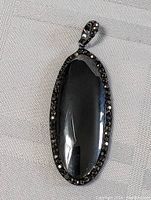 Front angled view of the oval black spinel pendant bordered with smaller black stones.