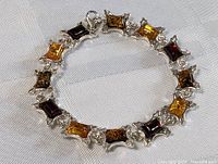 Full view of the circular sterling silver bracelet displaying alternating amber stones in shades of honey, dark brown, and reddish tone, each set in decorative silver frames.