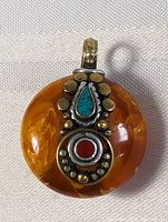 Photo of the front of the pendant showing amber resin circular base with sterling silver overlay featuring turquoise and coral stones accented by gold-tone button details.