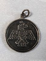 Front of round silver pendant with engraved Haida Thunderbird design and patina