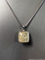 Close-up front view of the sterling silver necklace showing the square jadeite pendant with golden rutilated inclusions enclosed in silver setting.