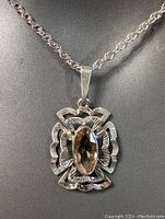 Close-up of the pendant shows detailed carving and the oval stone in yellowish setting.