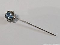 Side view of sterling silver stick pin showing the thin shaft and aqua tone gemstone.