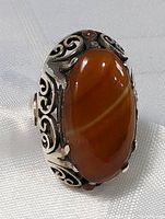 Close-up image showing the large polished oval brown tourmaline stone set in an ornately designed sterling silver band with scroll and swirl detailing.