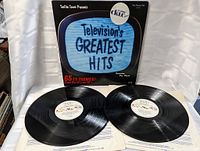Photo showing the album cover with TV graphic and two vinyl records in front with labels visible and original sleeves underneath.