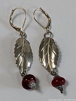 Pair of sterling silver dangle earrings with leaf designs and one with a red bead.