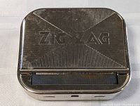 Top view showing embossed Zig-Zag logo on ribbed textured metal surface of cigarette case.