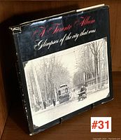 Front view of the book with black dust jacket showing the title 'A Toronto Album: Glimpses of the city that was' and a vintage street view of Toronto with a streetcar and a person on a sled.