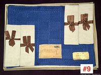 Full view of six-piece set with two blue placemats and four white napkins tied with brown ribbons in original box, showing unopened condition and vintage labels.
