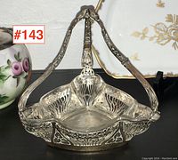 Front three-quarter view of triangular silver basket with raised handle and pierced floral design.