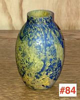 Front angle of blue and yellow mottled art glass vase with oval form and cylindrical neck.