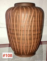 Front and slightly angled view of the carved terra cotta pot with vertical and curved linear engravings visible on warm brown surface.