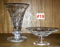 Photo showing front view of cut crystal vase and small pedestal dish on wooden background with lot number #19 visible