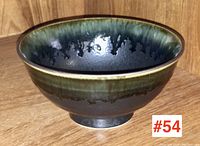 Studio art pottery bowl with dark green, black, and brown glaze, side angle showing shape and foot of the bowl.