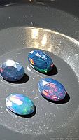 Four oval faceted Ethiopian black opal gemstones showing bright multicolor flash including red, blue, green, and orange on black body tone.