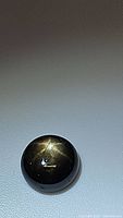 Close-up photo of a round cabochon black star sapphire showing a bright 6-ray star asterism on its surface under light.