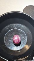 Oval cabochon cut natural star ruby gemstone showing 6-ray star effect under light, polished, deep reddish color with natural inclusions.