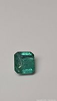 Close-up photo of the emerald showing rectangular cut, green color with internal inclusions and surface reflection.