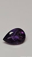 Close-up image of pear-shaped deep purple amethyst gemstone showing facets and clarity.