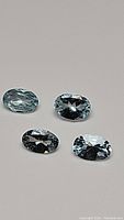Photo showing four oval cut natural untreated Brazilian aquamarines varying slightly in size and color tone on neutral background.