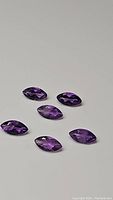 Six marquis cut, faceted amethyst gemstones laid on a white surface showing their deep purple color and clarity.