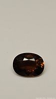 Oval cut cognac colored tourmaline gemstone on plain background showing facets and color