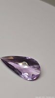 Top view of the pear-shaped checkerboard cut purple pink amethyst gemstone showing its transparent and faceted surface.