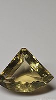 Close-up of yellow lemon-colored gemstone with fancy cut, multiple facets, triangular shape.