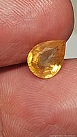 Close-up of the pear-shaped golden yellow sapphire held between fingers showing color and cut.
