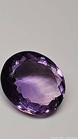 Close-up of 11.59 carat natural oval cut deep purple amethyst showing facets and clarity with slight inclusions visible.