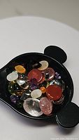 Photo of a black tray filled with various natural faceted and cabochon gemstones in multiple colors including red, purple, green, orange, and clear hues.