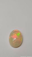 Close-up photo of oval cabochon Ethiopian opal showing bright flashes of green, orange, and red colors on a translucent white base.