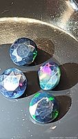 Four round calibrated 5mm natural black opal gemstones shown together, highlighting their rainbow flashes and faceted diamond cut style.