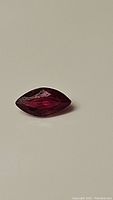 Close-up photo of a single marquis cut blood red ruby gemstone on a neutral background.