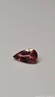 Close-up photo of pear shaped natural pink tourmaline gemstone showing internal clarity and bright pink hue against a neutral background.