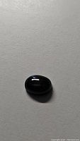 Natural black oval cabochon star diopside gemstone shown under diffuse light showing smooth polished surface and deep black color.