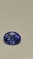Close-up photo of a natural oval cut Tanzanite gemstone with visible internal inclusions and purple-blue color.