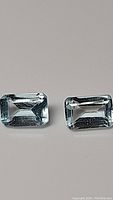 Photo of two emerald-cut natural sky blue topaz gemstones side by side on a neutral background.