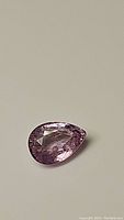Pear-shaped pastel pink to purple sapphire gemstone on neutral background, showing internal facets and clarity.