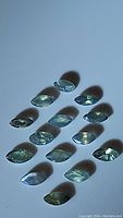 Fourteen natural marquis cut alexandrite gemstones arranged on a flat surface showing green-blue shades.